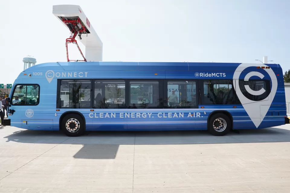Blue electric MCTS bus sits at a charging station